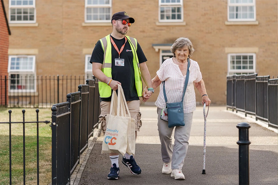 Community Connections worker supporting mature person from transport with shopping